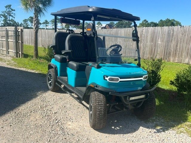 Blue and black golf cart parked on a gravel driveway beside a wooden fence and green lawn.