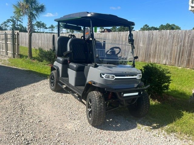 Black golf cart parked on a gravel driveway beside a wooden fence on a sunny day