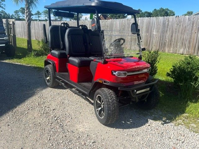 Red golf cart parked on gravel beside a wooden fence in a sunny yard.