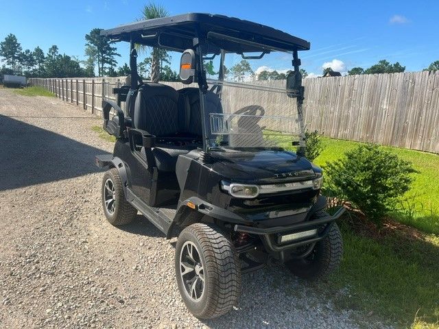 Black four-seat utility golf cart parked on a gravel path beside a wooden fence and hedge.