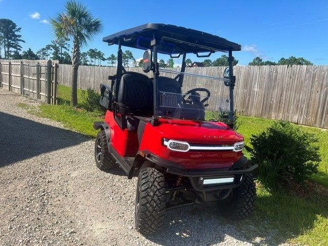 Red golf cart with black roof parked on gravel beside a wooden fence in a sunny yard
