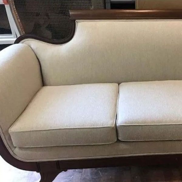 Cream upholstered sofa with two seat cushions and dark wood trim, shown close up indoors