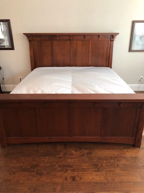 Wooden bed with white bedding in a bedroom with hardwood floors and framed pictures on the walls