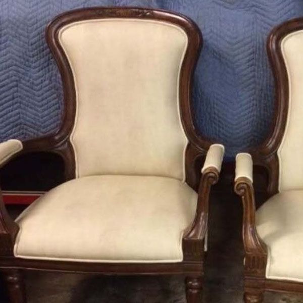 Two upholstered cream-and-wood armchairs on a blue quilted blanket background