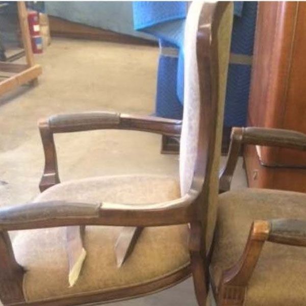 Two wooden armchairs with beige cushions in a room, viewed closely from the side.