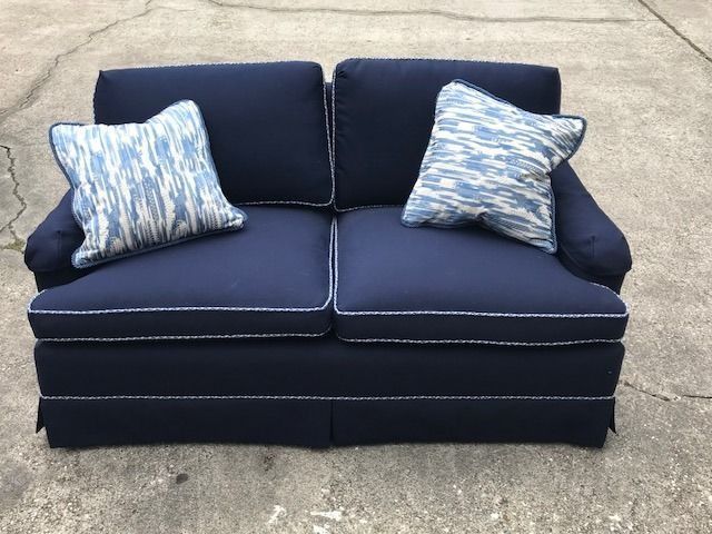 Navy blue loveseat with two patterned throw pillows on a concrete surface