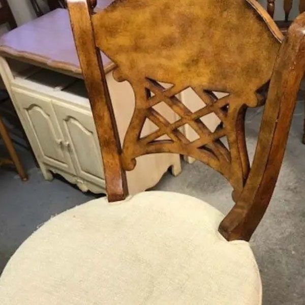 Close-up of a wooden chair with carved backrest and cream upholstered seat on a gray floor