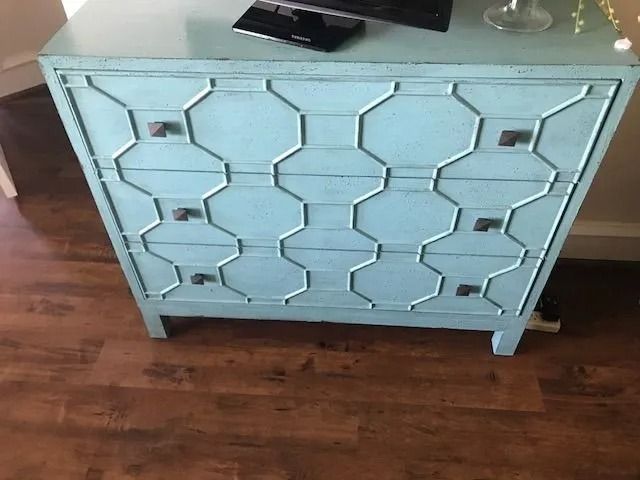 Light blue patterned dresser with drawers on a hardwood floor.