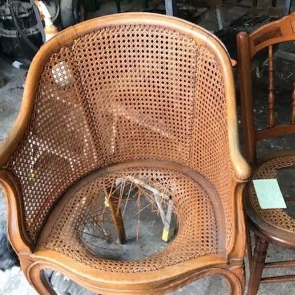 Wicker armchair with cane back and seat, showing a large hole in the seat