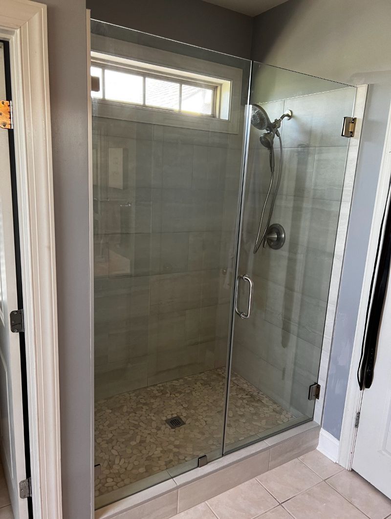 A bathroom with a walk in shower with a glass door and a window.