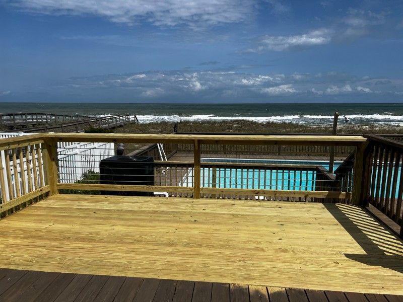 A wooden deck with a view of the ocean and a swimming pool.