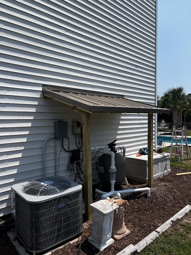 An air conditioner is sitting under a canopy on the side of a house.