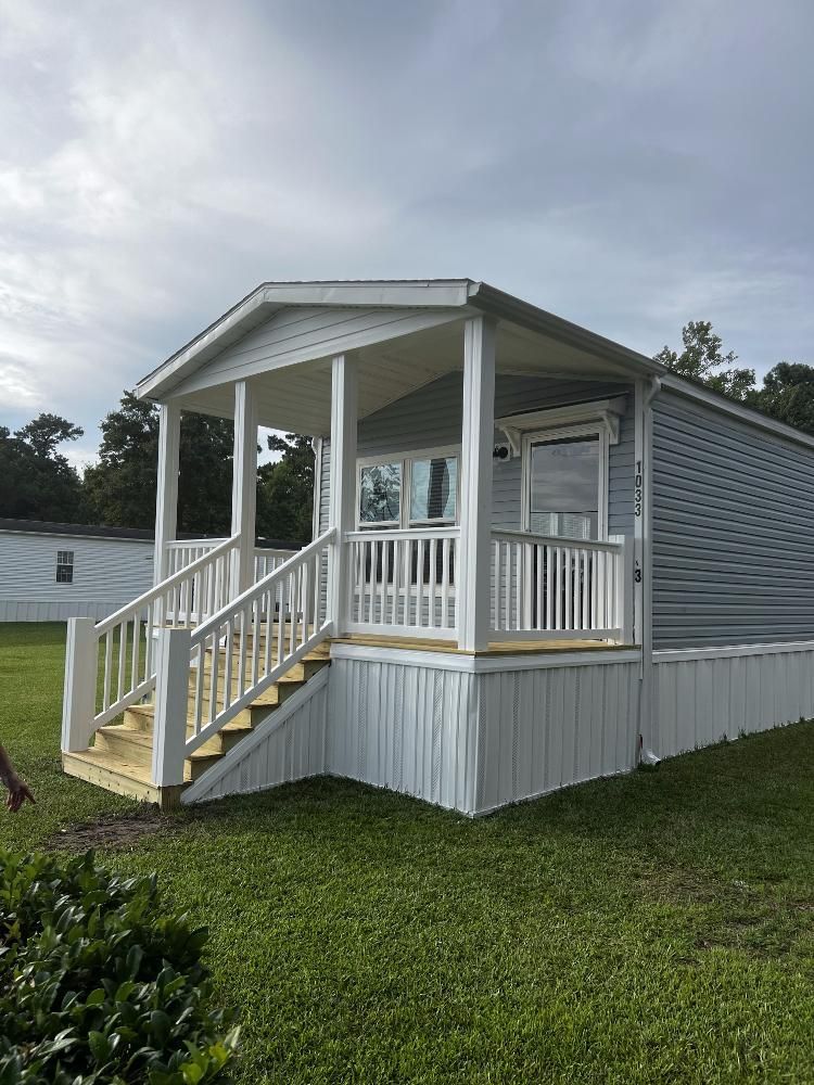 A mobile home with a porch and stairs in a grassy field.
