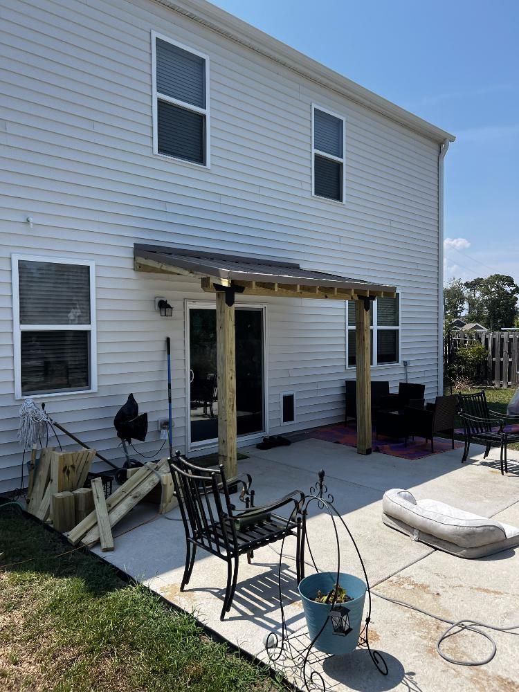 A white house with a wooden pergola on the back patio.