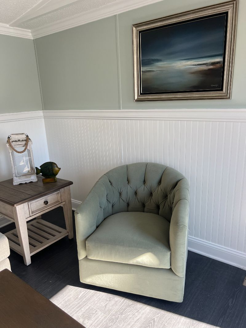 A living room with a chair , table , and painting on the wall.