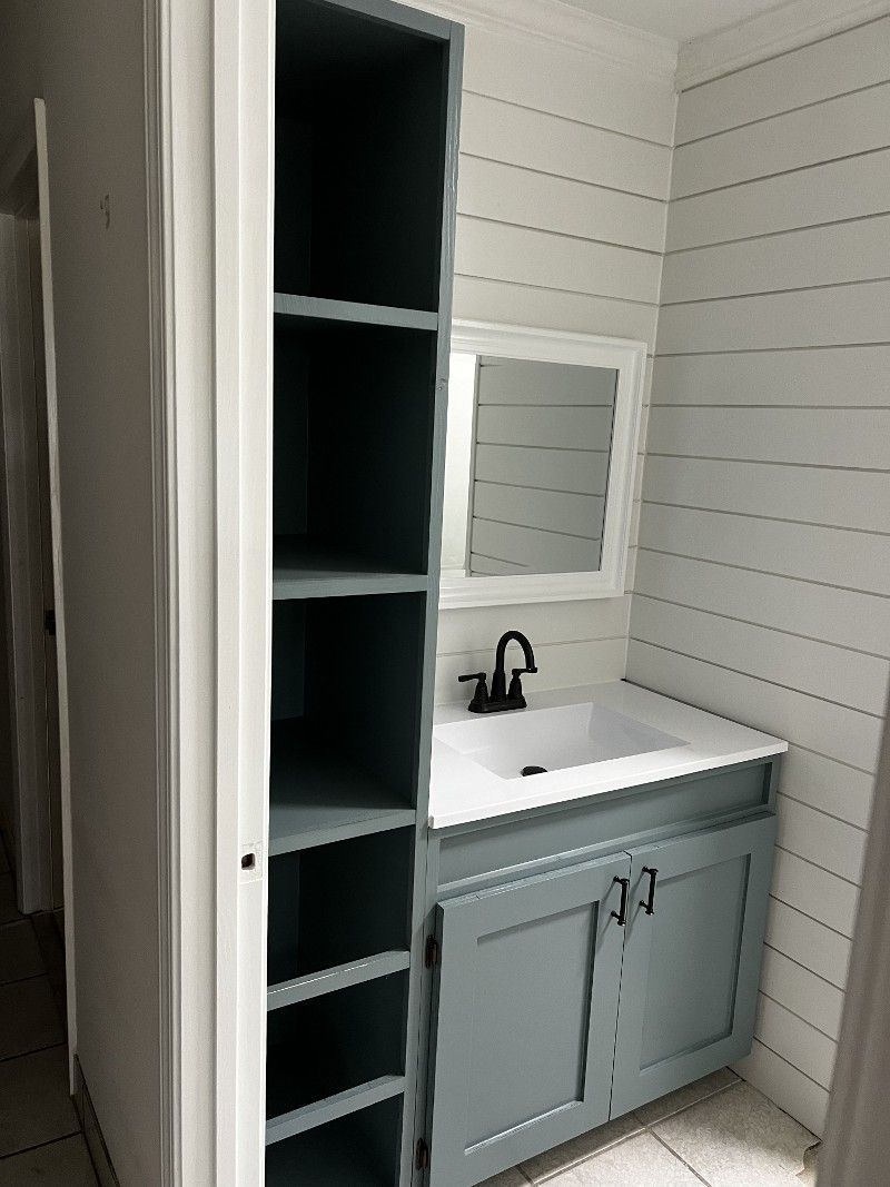 A bathroom with a sink , mirror and shelves.