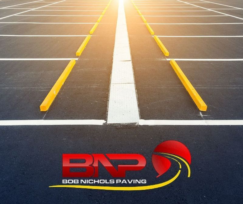 Empty parking lot with yellow wheel stops, white lane markings, and the Bob Nichols Paving company logo.