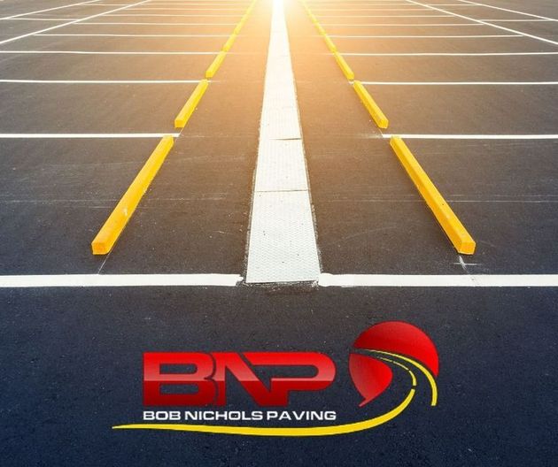 Empty parking lot with yellow wheel stops, white lane markings, and the Bob Nichols Paving company logo.