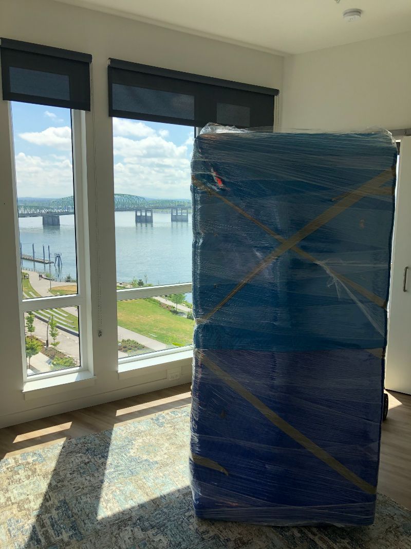 A large blue box is wrapped in plastic in a room with a view of the water.