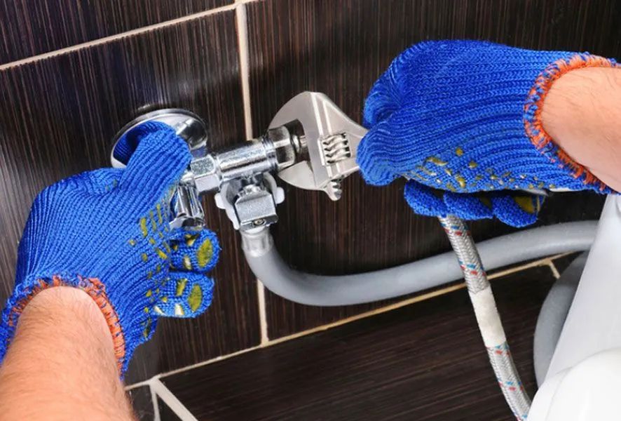 Plumber wearing blue gloves using a wrench to work on plumbing.