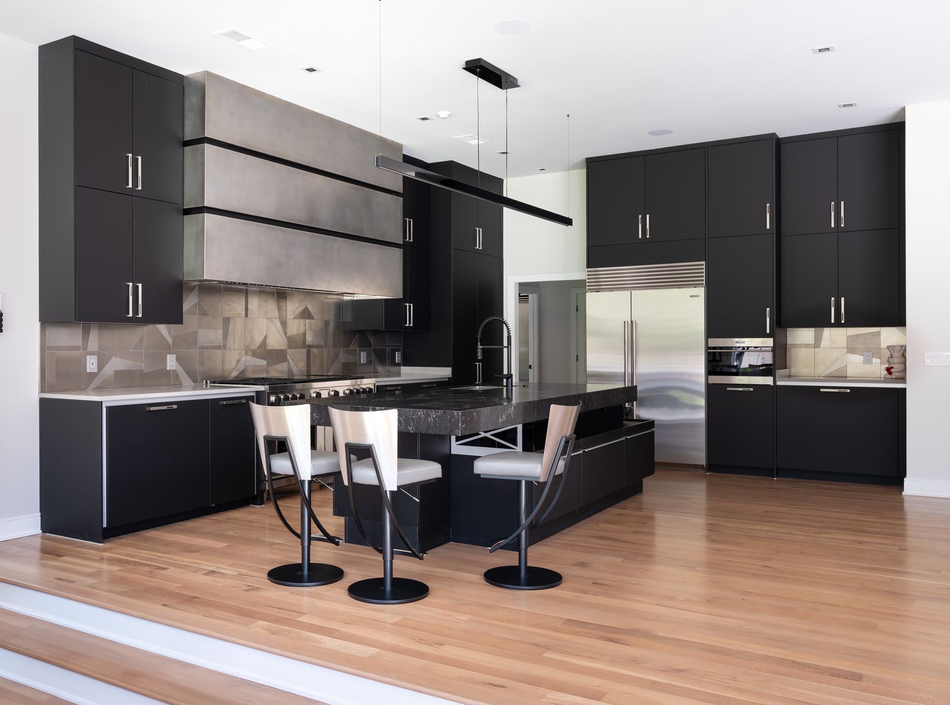 Modern kitchen with black cabinets, stainless steel appliances, wooden floors, and an island with seating.