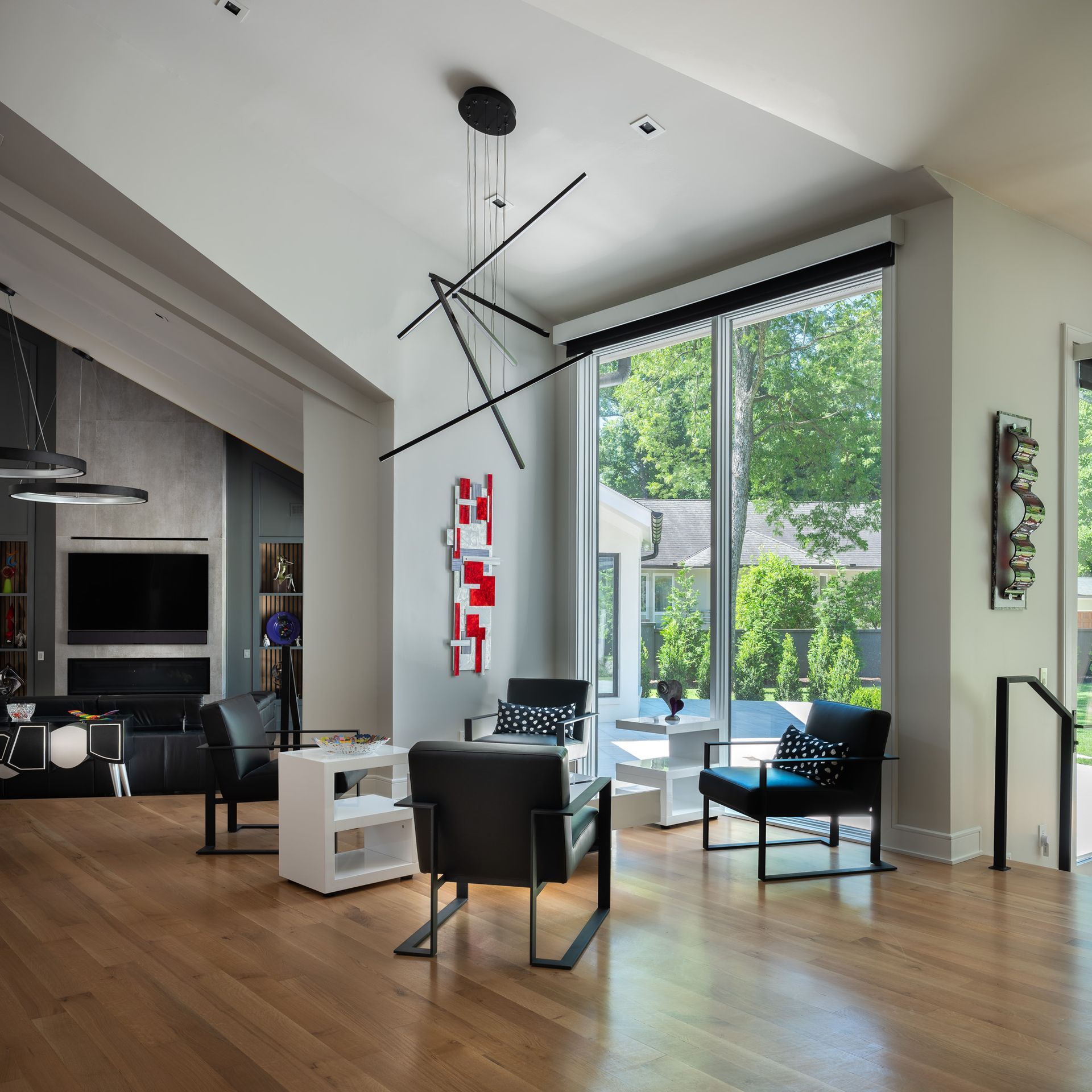 Modern living room with black chairs, white tables, large window, and a unique geometric light fixture.