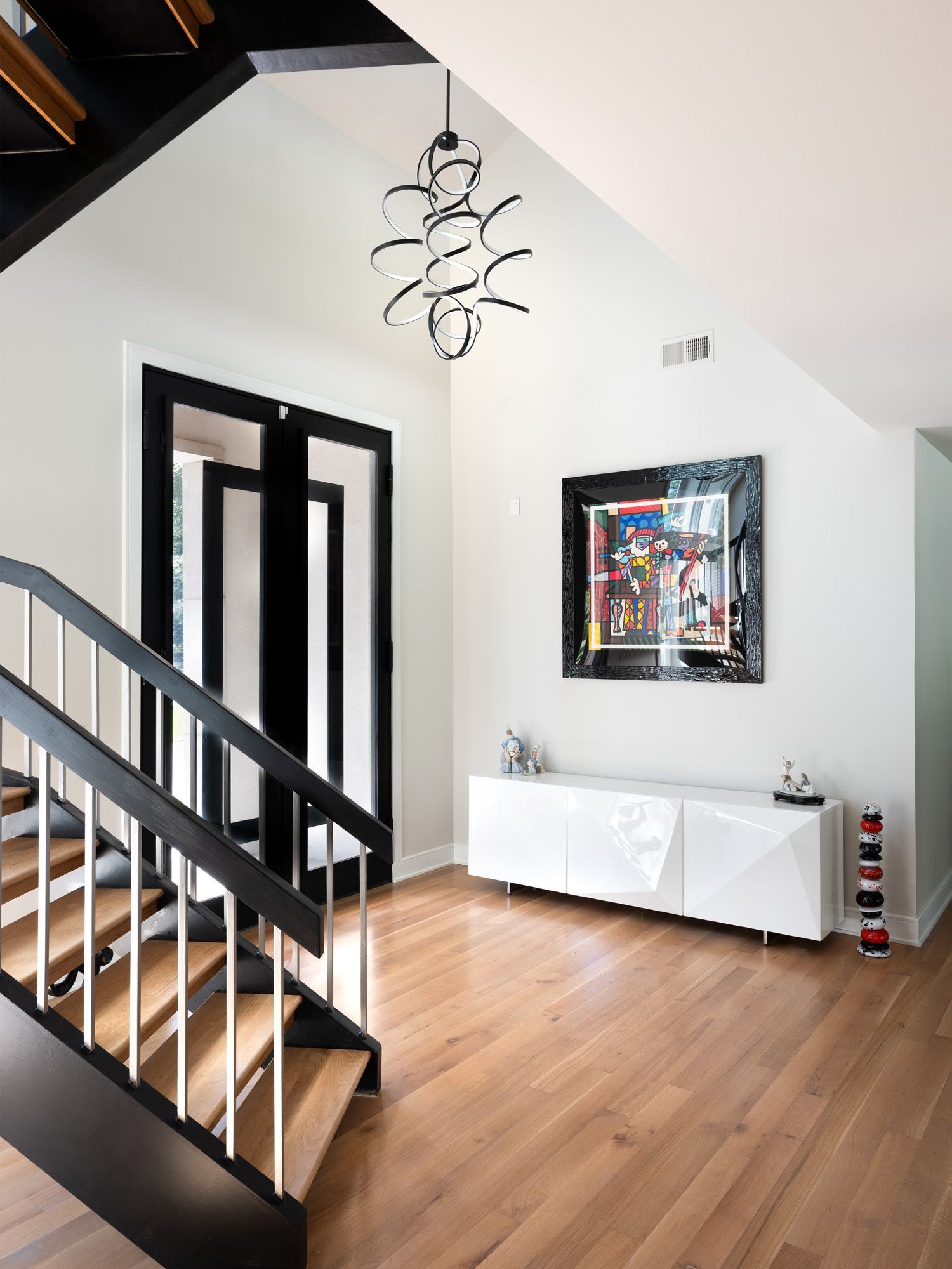 Modern foyer with wooden floor, white walls, black framed doors and stairs, and abstract art.