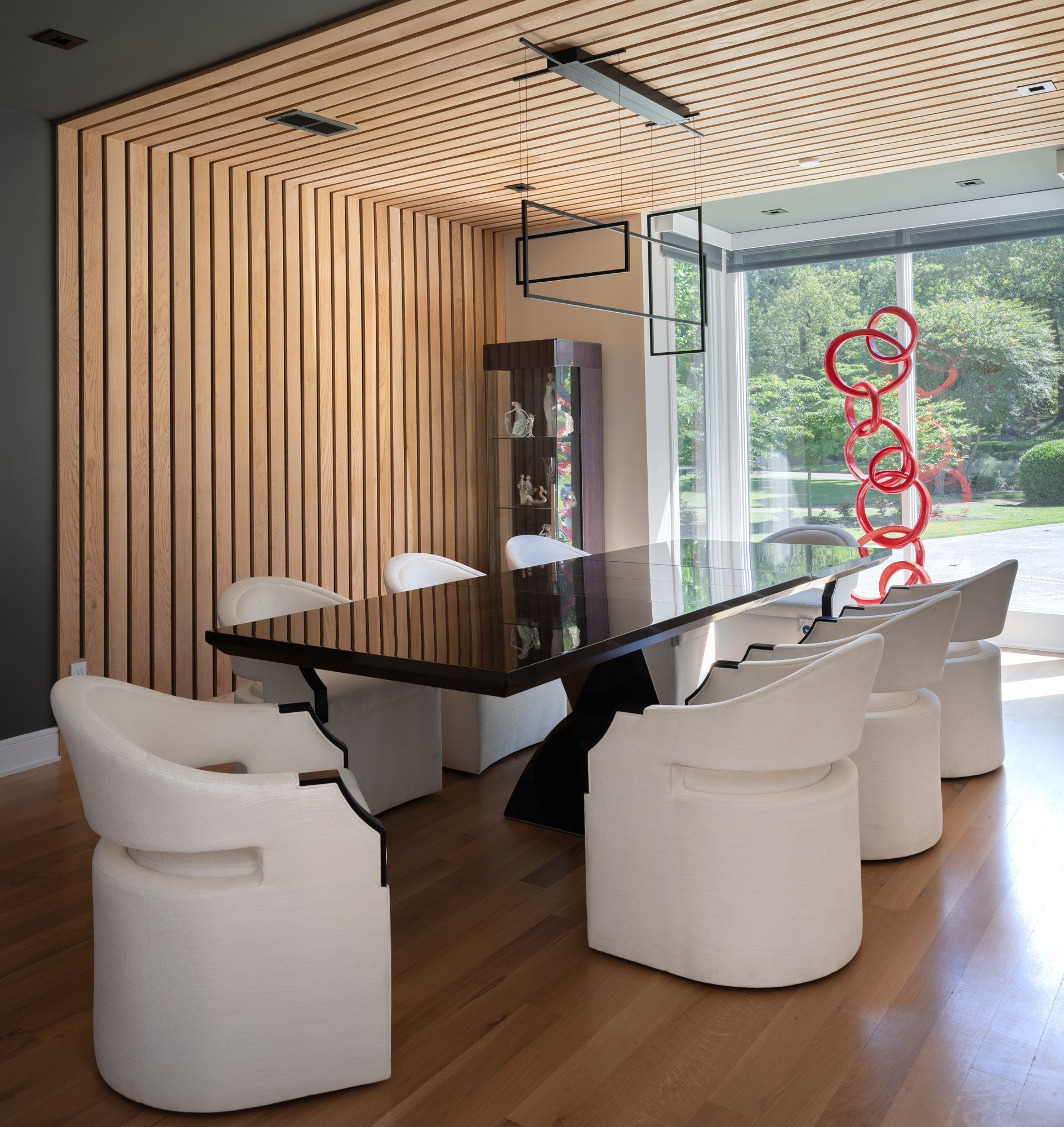 Dining room with wooden slatted wall, dark table, white chairs, and art.