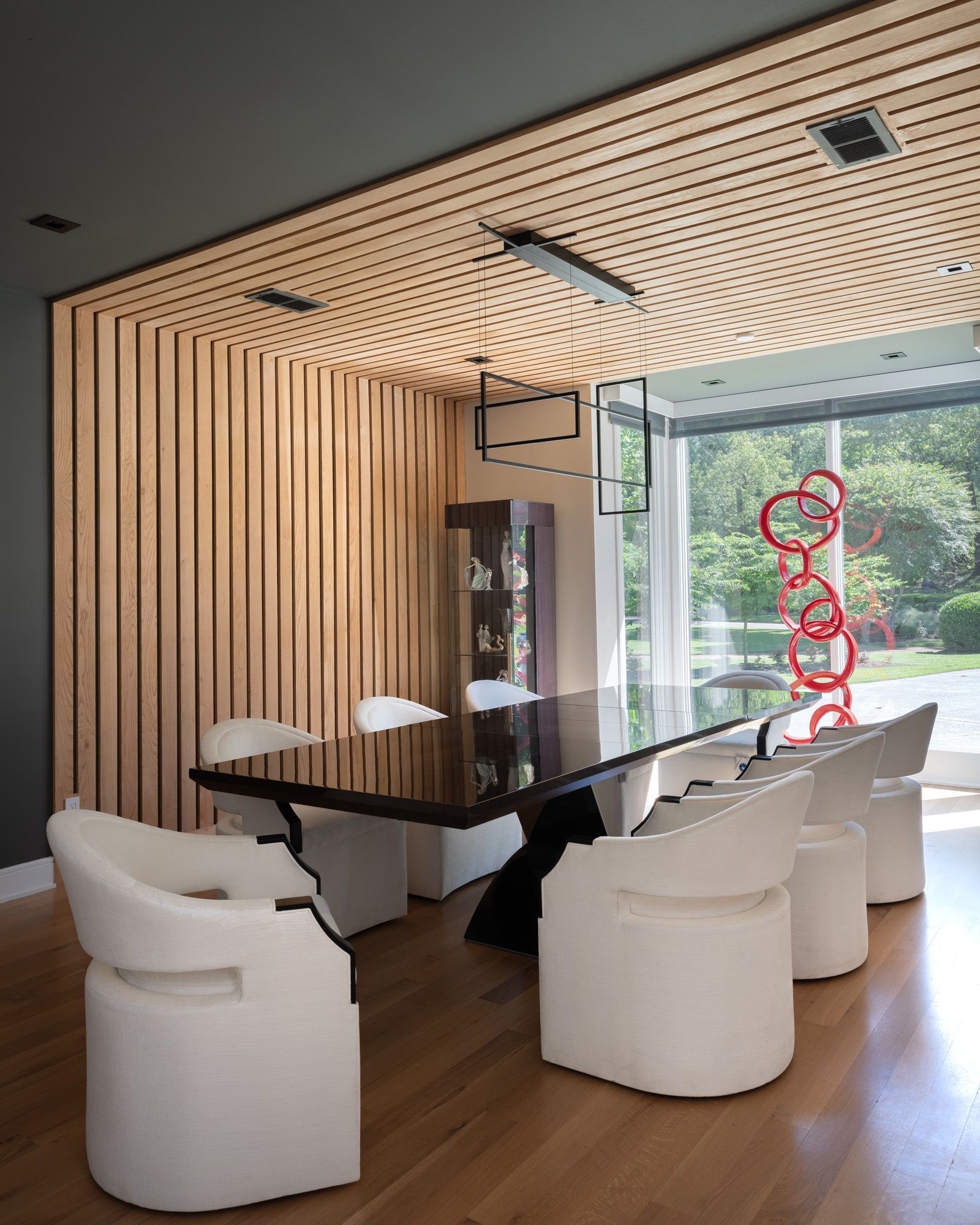 Modern dining room with long black table, white chairs, wood paneling, and a large window.