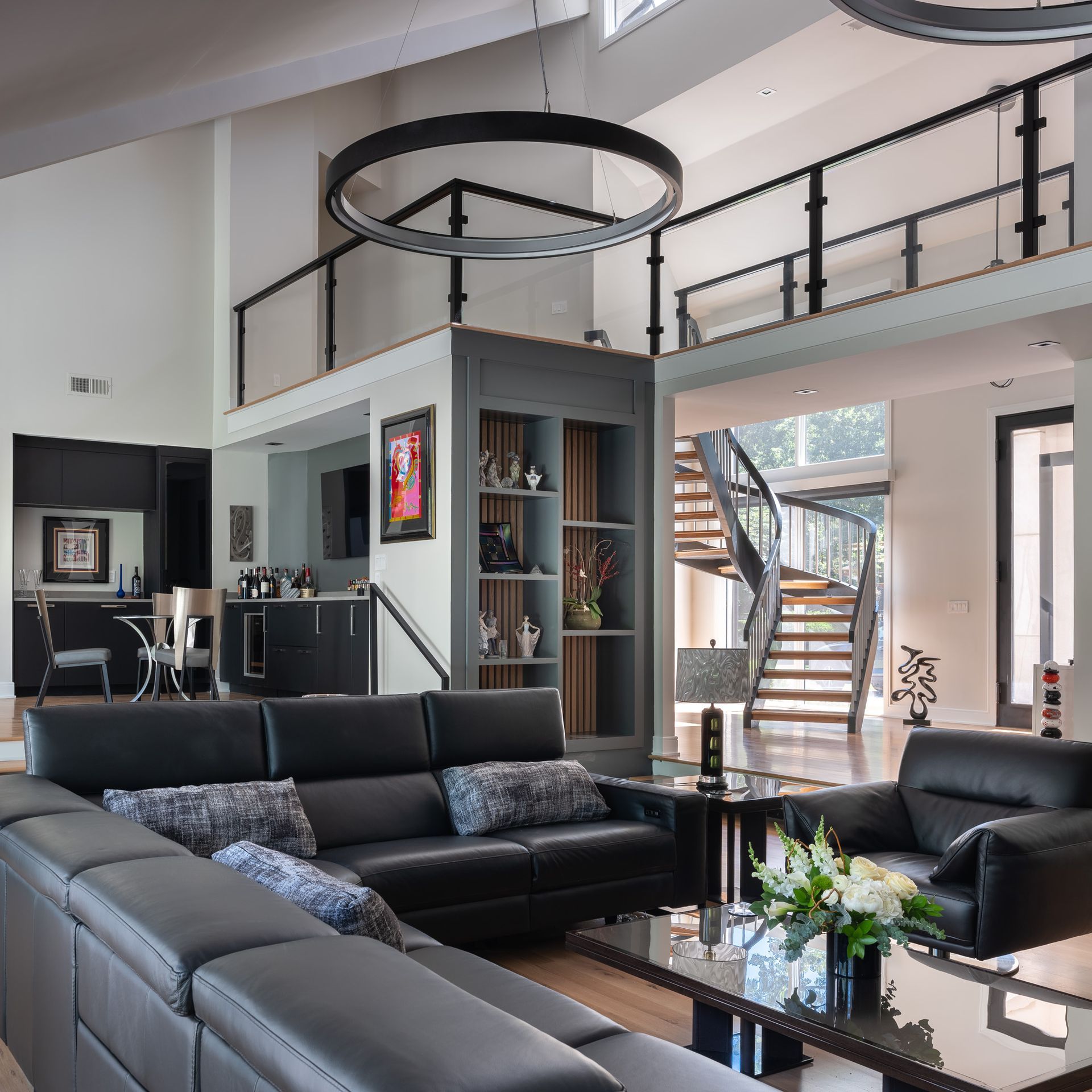 Modern living room with black leather furniture, spiral staircase, and loft.