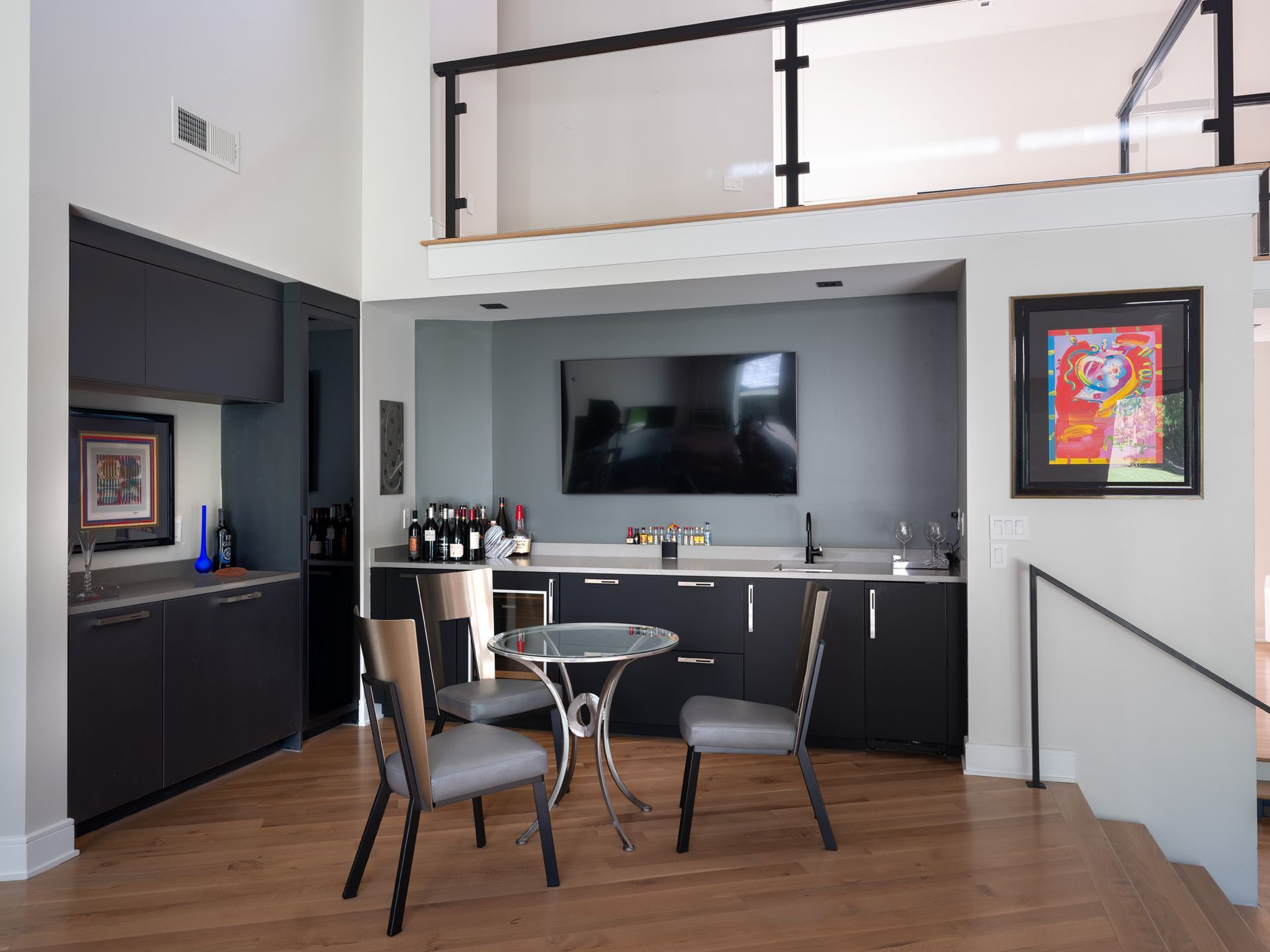 Modern home bar with a small table and chairs, a TV, and cabinetry.