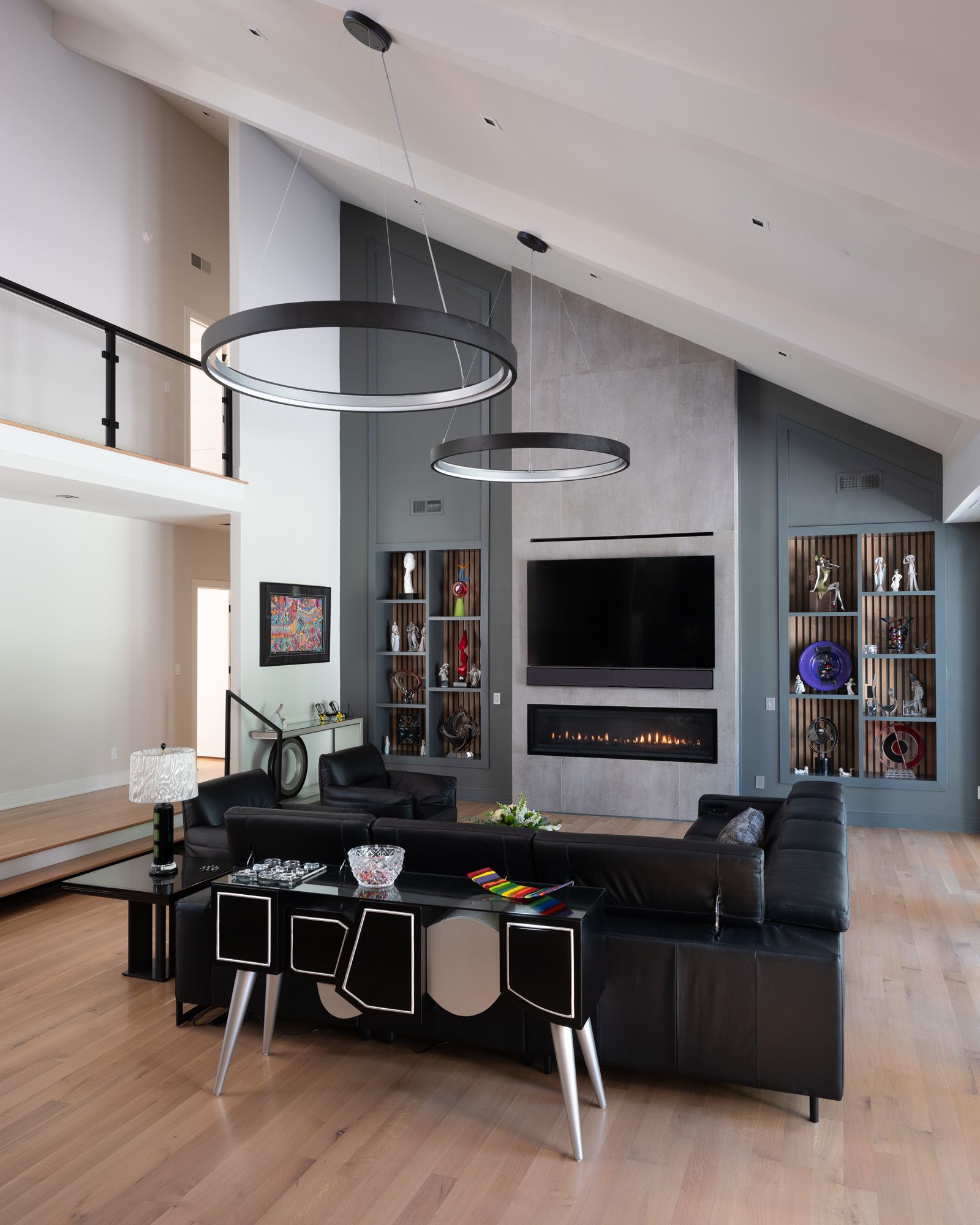 Modern living room with black furniture, fireplace, and circular pendant lights.