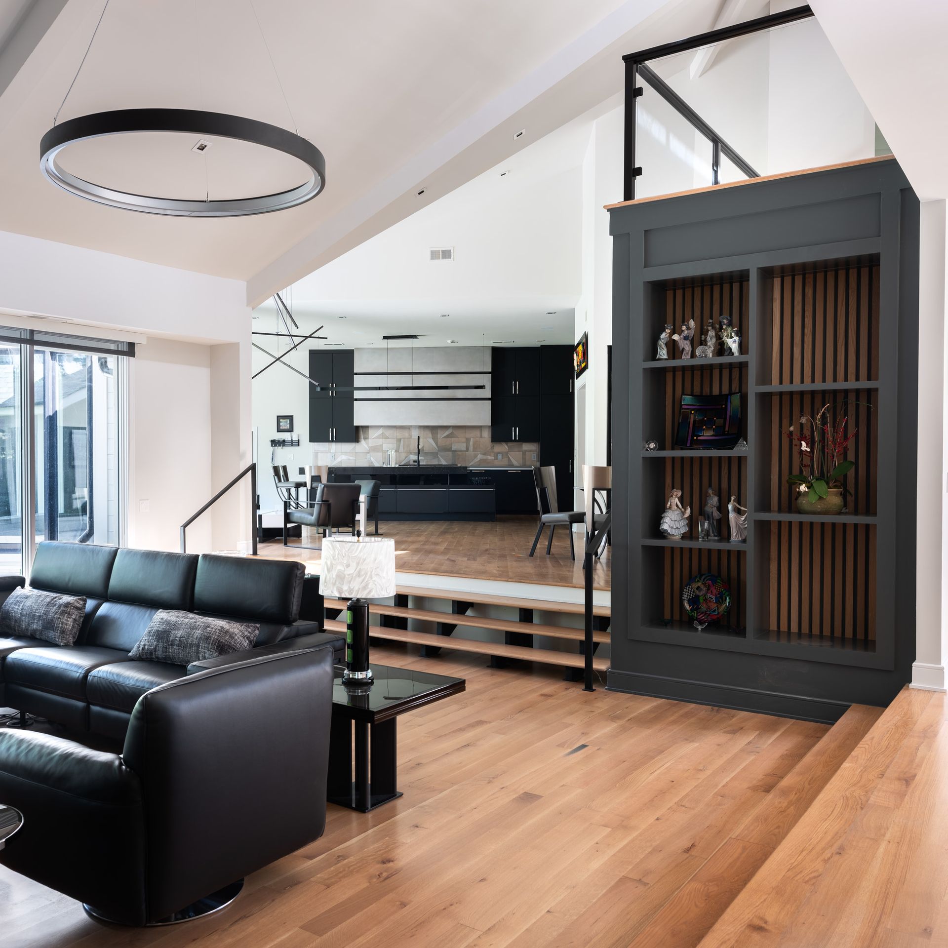 Living room with black leather sofa, dark gray bookcase, and open kitchen in background.