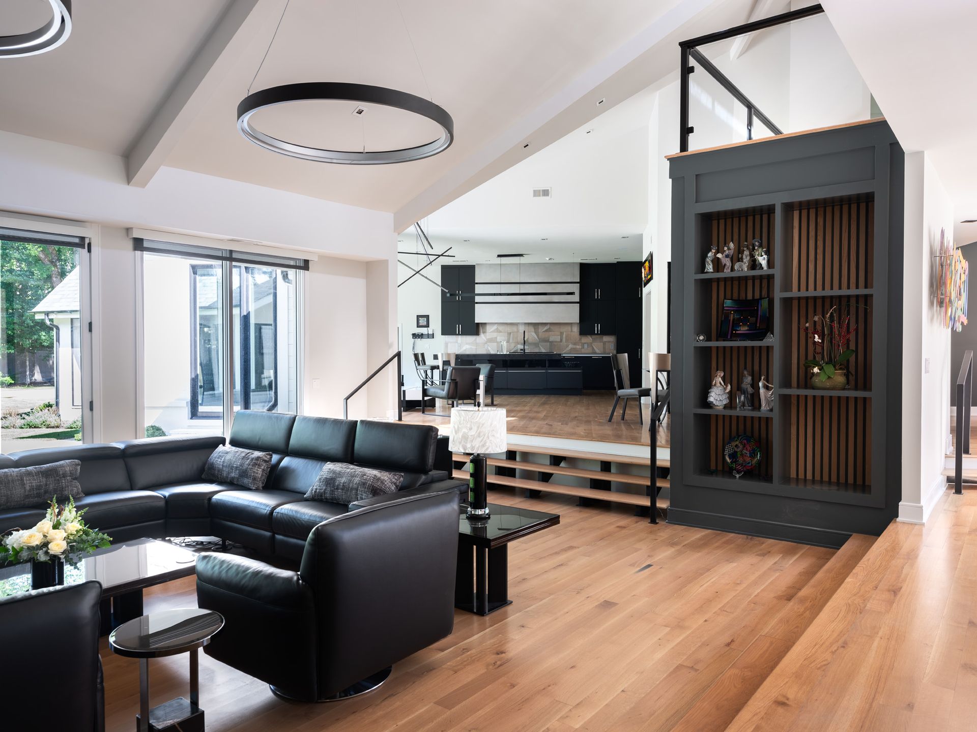 Spacious modern living room with black sectional, open kitchen, wooden floors, and a built-in display cabinet.