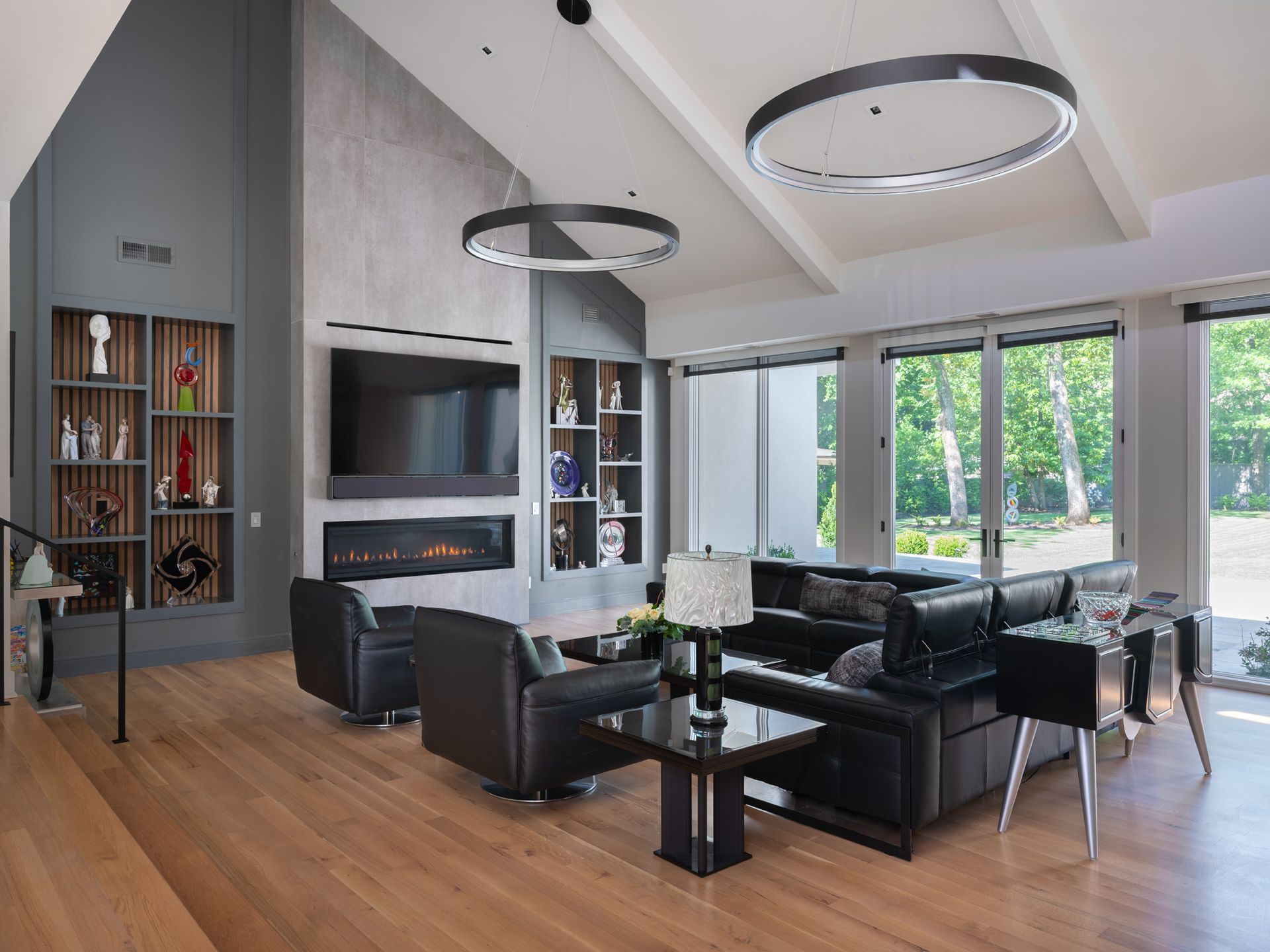 Modern living room with black leather furniture, fireplace, and large windows.