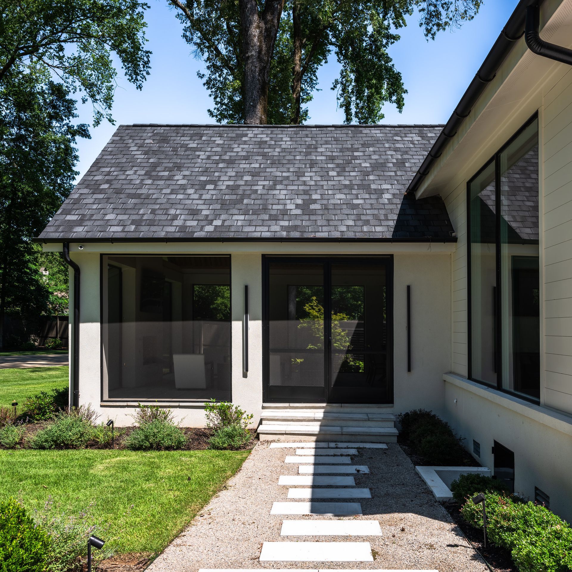 Exterior view of a white house with a pathway of stone slabs leading to the black entry door and screened windows.