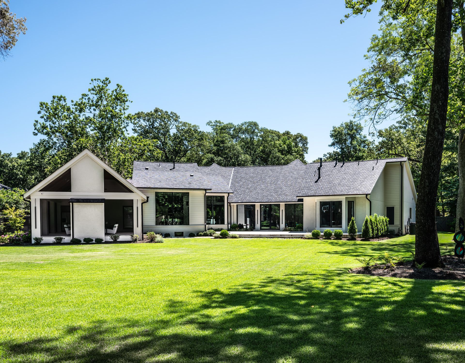 Backyard of a white house with glass doors and windows on a sunny day, with lush green lawn.