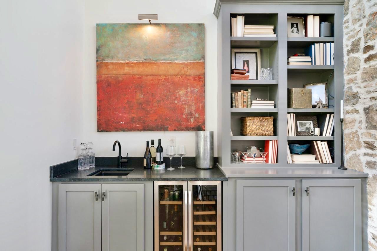Built-in grey bar with a sink, wine fridge, and bookcase, accented by an abstract painting.