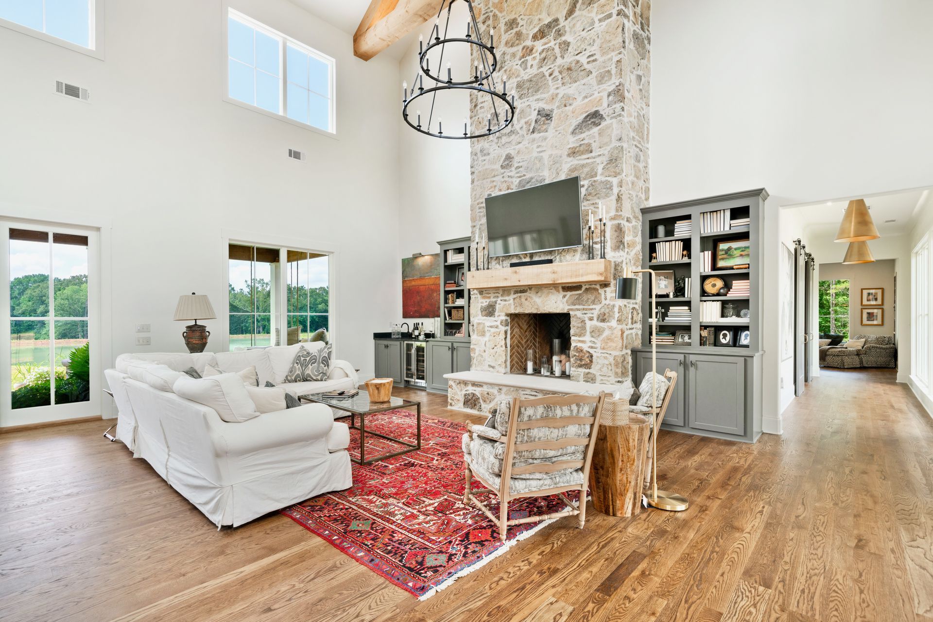 Spacious living room with stone fireplace, white sofa, red rug, and large windows with outdoor views.