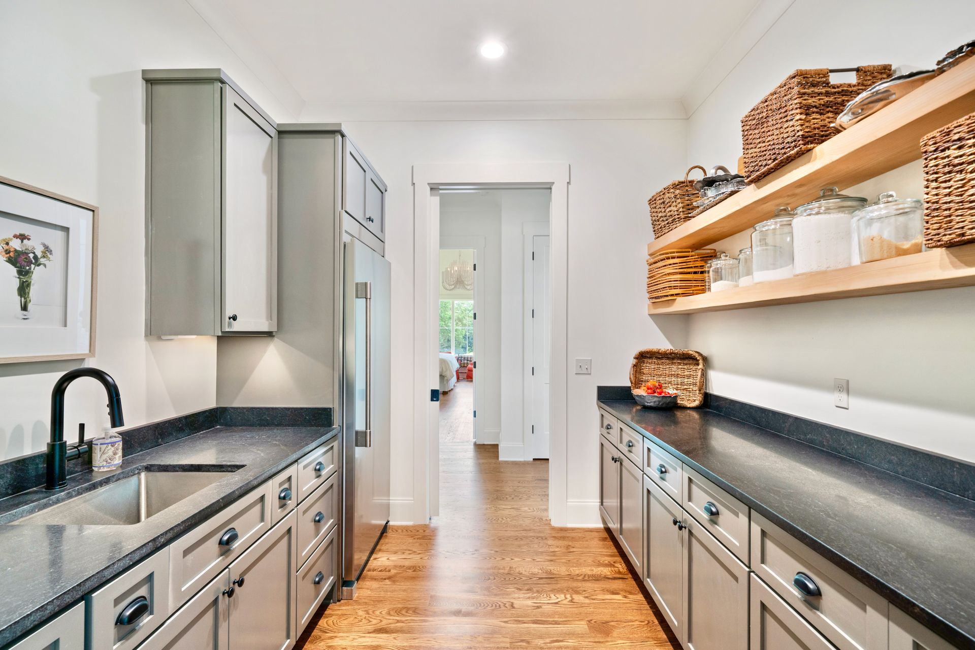 Pantry with gray cabinets, black countertops, and wooden shelves.
