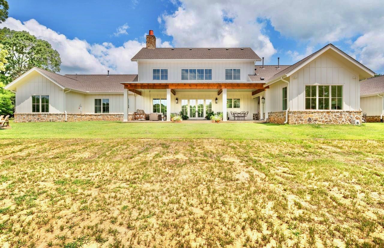 White farmhouse with a large backyard, blue sky, and clouds.