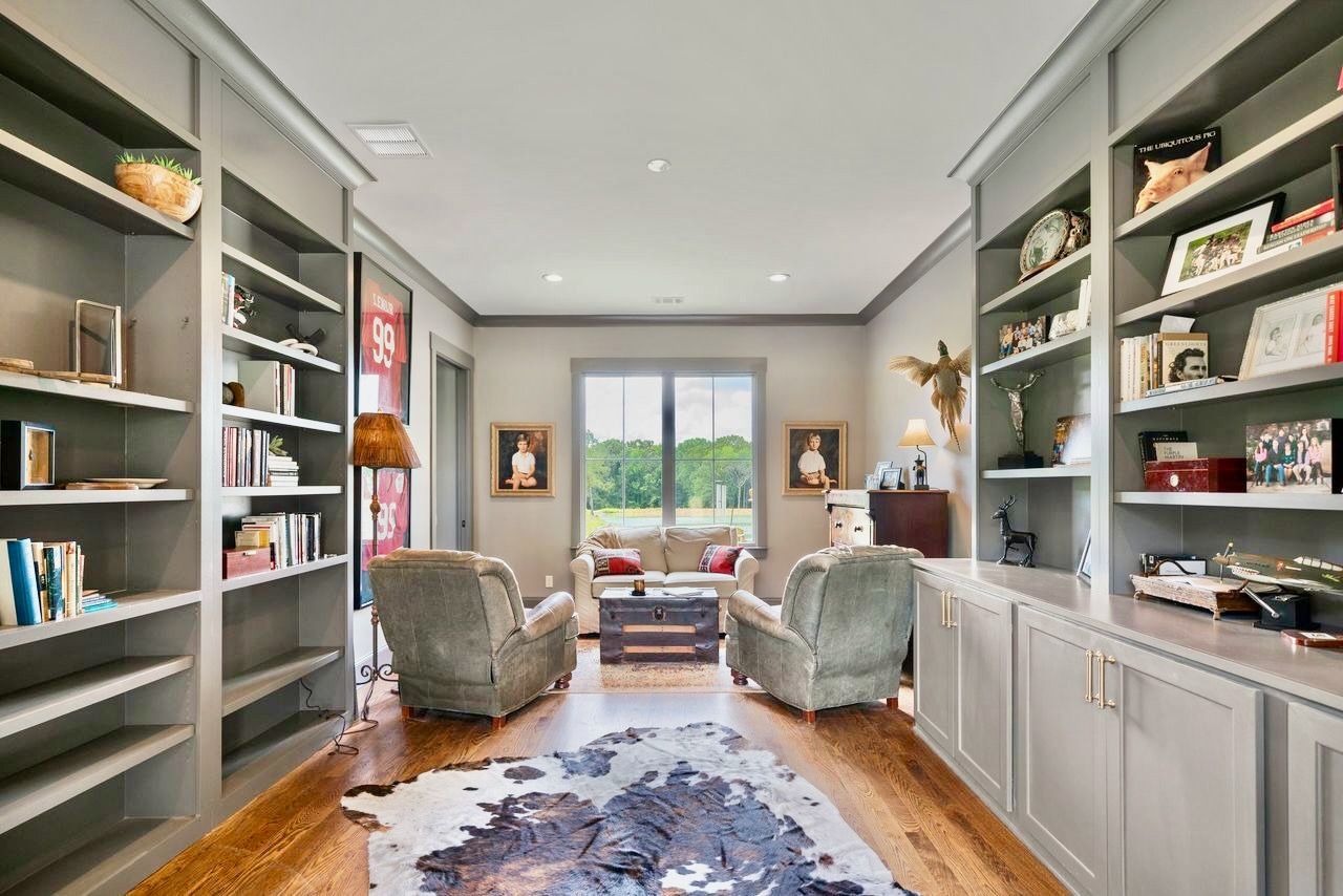 Cozy library with gray bookshelves, two armchairs facing a window, and a cowhide rug.