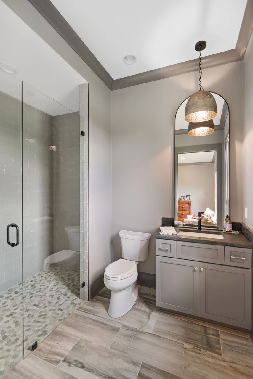 Bathroom with shower, toilet, vanity, and decorative lighting gray tones throughout.