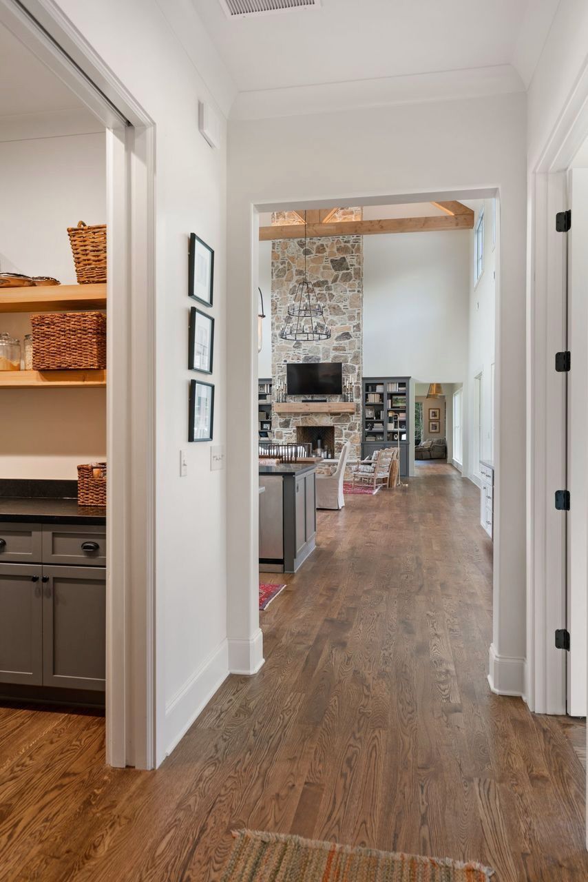 Hallway leading to a living room with stone fireplace, open pantry on left, dark wood floors.