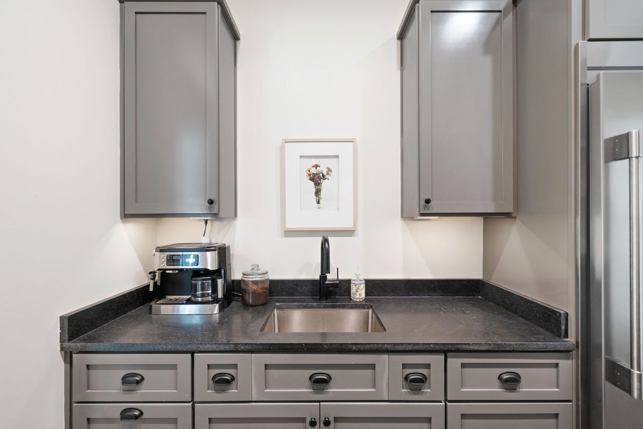 Gray kitchenette with cabinets, sink, coffee maker, and framed artwork.