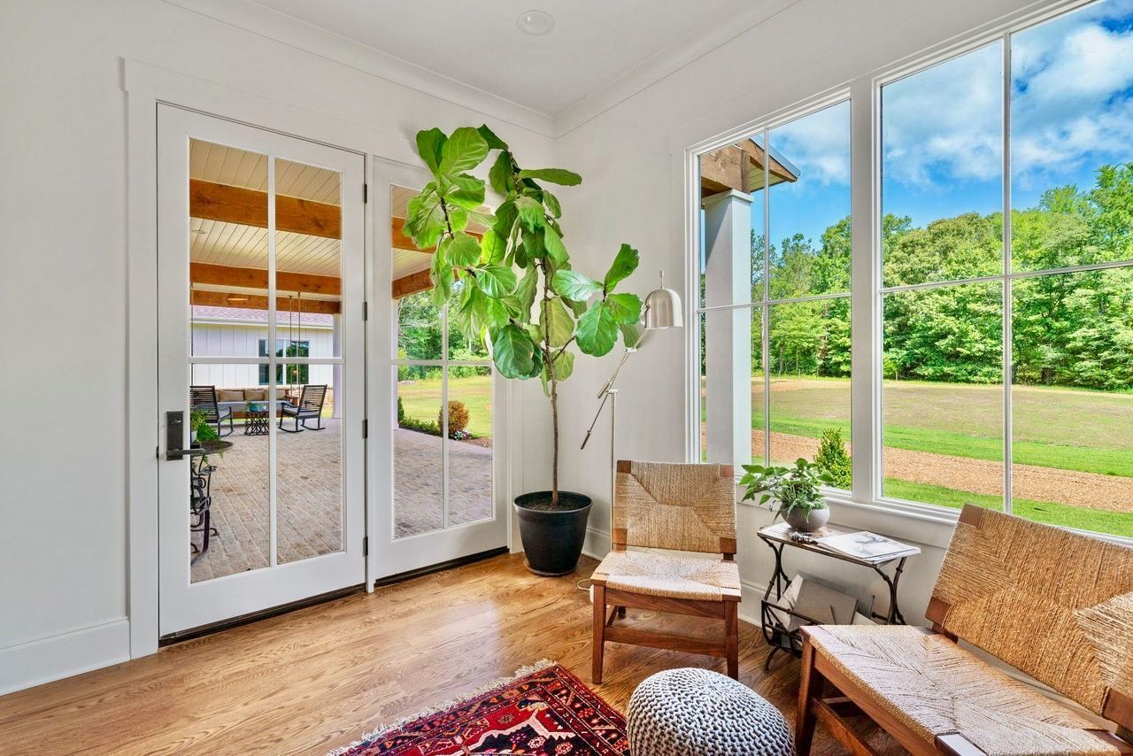 Sunroom with French doors, large window, potted plant, wicker chairs, and outdoor view.