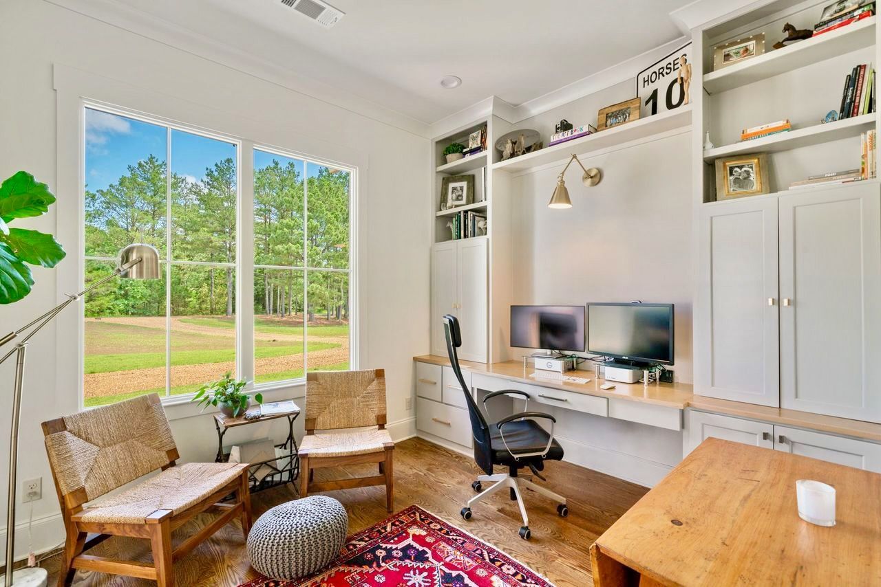 Home office with built-in desk, two chairs, large window overlooking a yard.