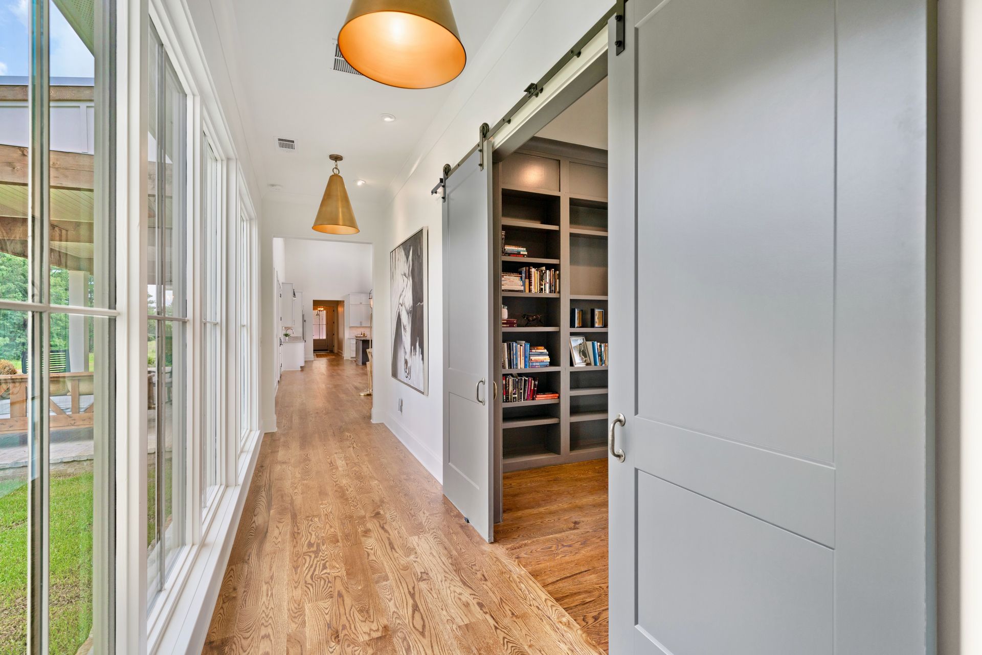 Long hallway with hardwood floors, a sliding door to a library, and windows to the left.