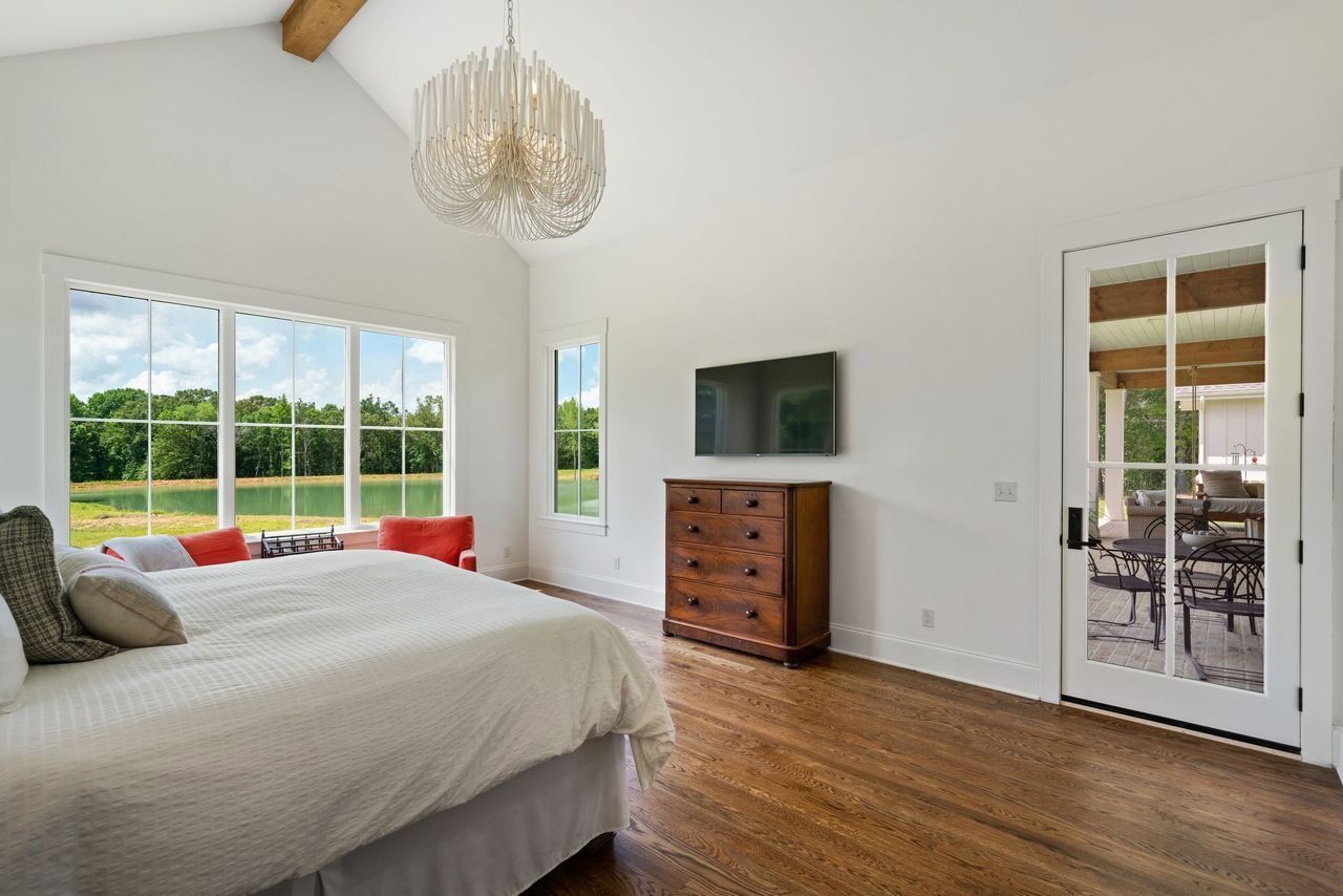 Bedroom with bed, dresser, window overlooking greenery, and a chandelier.