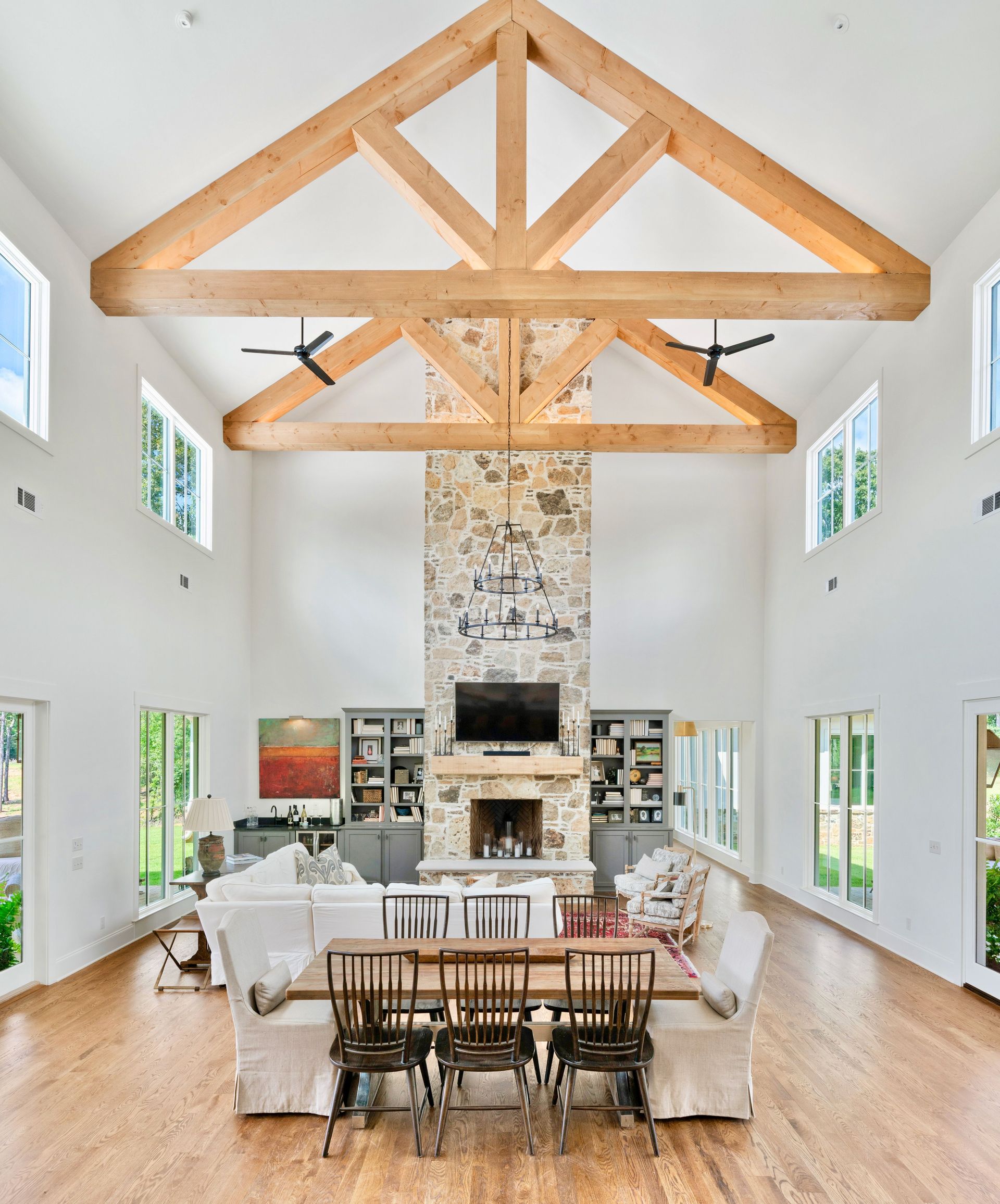 Spacious living room with vaulted ceiling, wooden beams, stone fireplace, and light-colored wood floor.